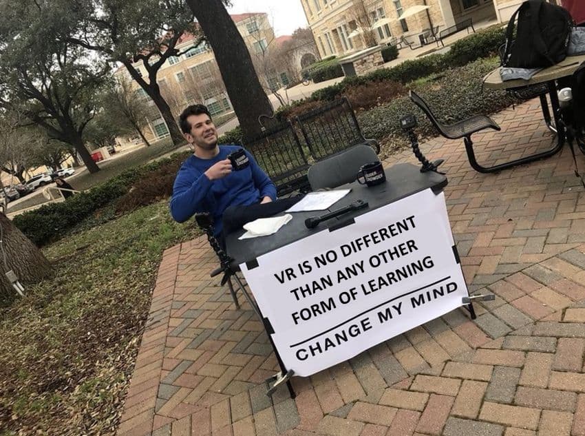 Photo of man with poised coffee mug sits at plain outdoor table with poster. Text: VR is no different than any other form of learning. Change my mind.