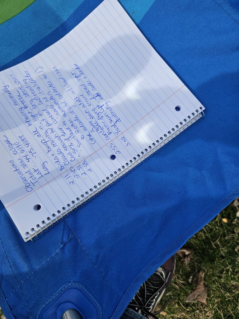 Photo of partial eclipse coming through binoculars showing a crescent shaped sun. The image was taken safely and is cast upon hand written notes.