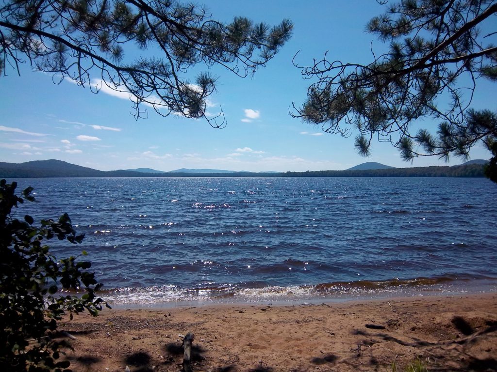 Photo of Lake Meacham, New York with the blue waters of the lake surrounded by the rounded Adirondack Mountains.